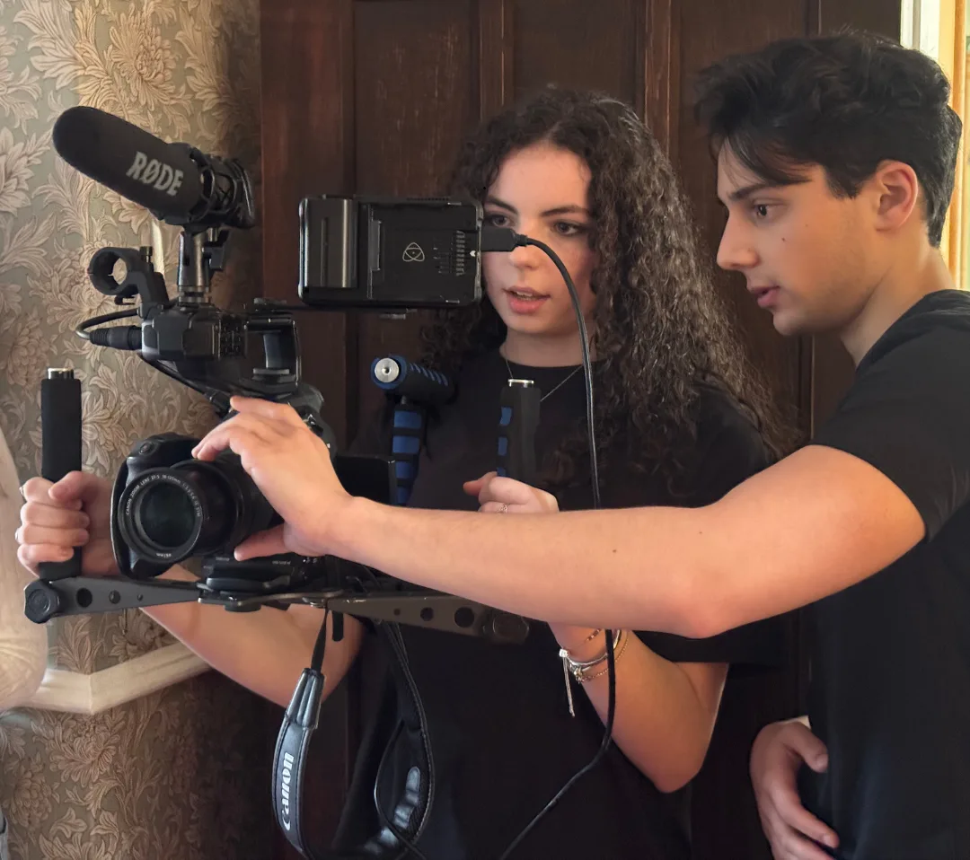 Two young people working together on a camera fitted with a shoulder rig, a Rode microphone and an external monitor