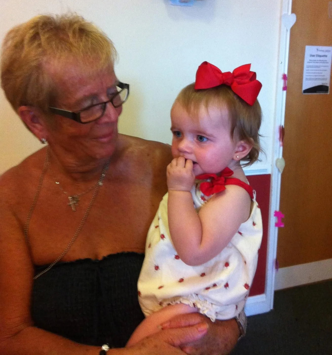 A woman in glasses holding a baby girl with a large red bow in her hair